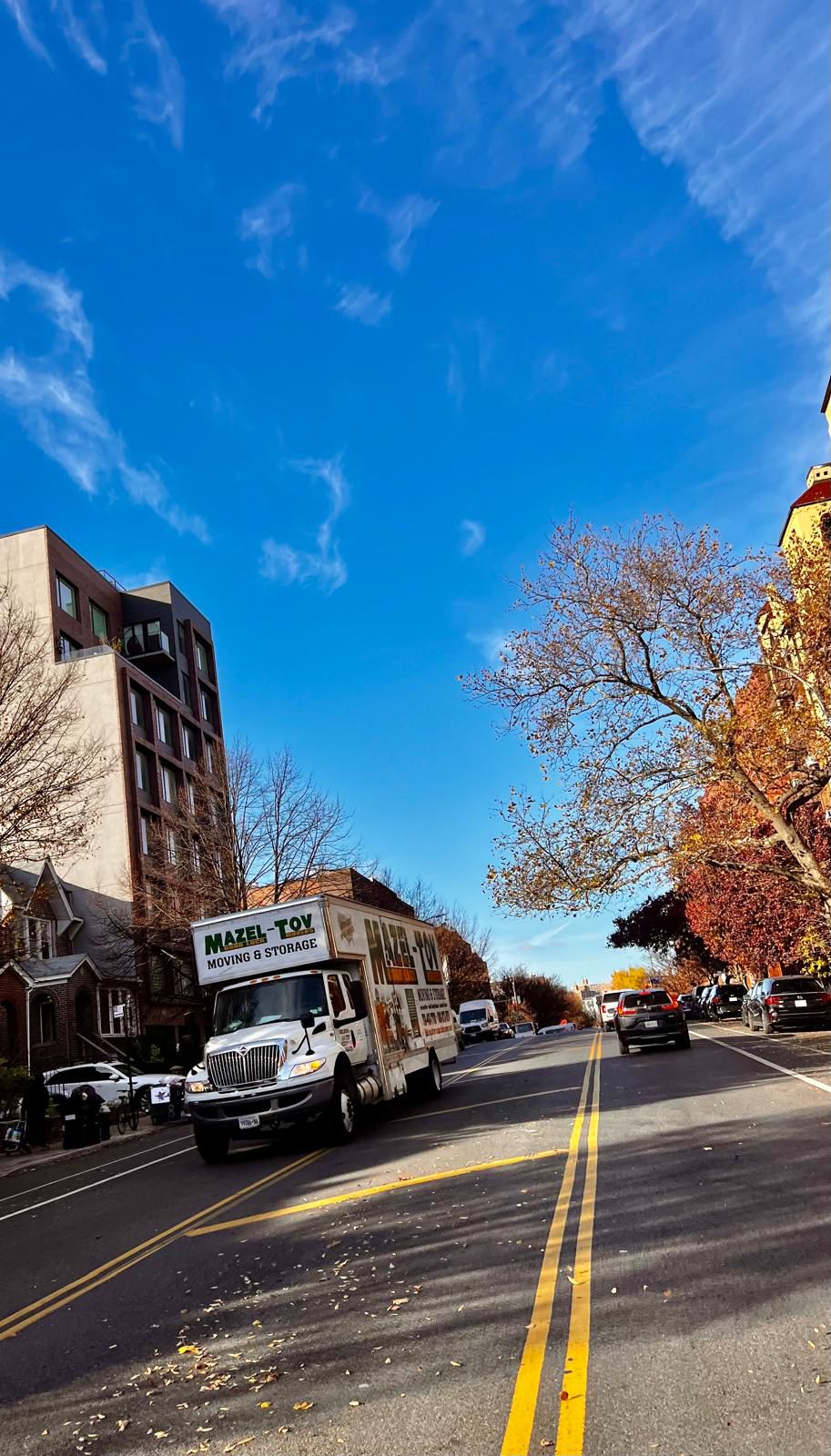 Mazel-Tov Movers truck driving down a tree-lined Brooklyn street